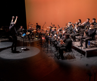 “Concierto de big band: director y sección de metales en el escenario.”